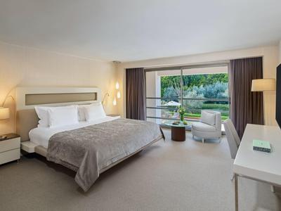 Modern eingerichtetes Hotelzimmer mit großem Bett und Blick auf eine grüne Außenanlage.