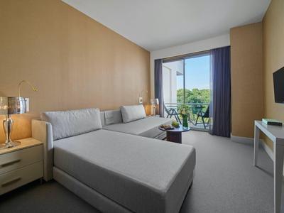 Modernes Hotelzimmer mit großem Bett, Sofa, TV und Zugang zu Balkon mit grüner Aussicht.
