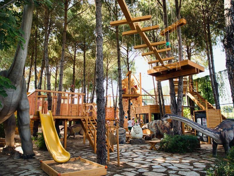 Ein großer Abenteuerspielplatz mit Rutschen und Klettergerüsten in einem bewaldeten Bereich.