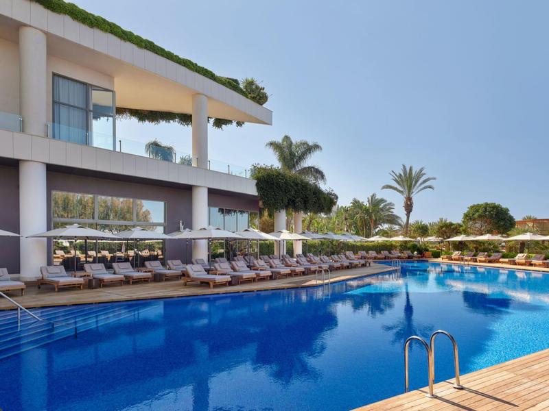 Moderner Hotelpool mit Liegestühlen und Palmen unter blauem Himmel