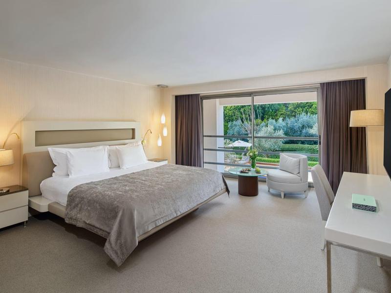 Modern eingerichtetes Hotelzimmer mit großem Bett und Blick auf eine grüne Außenanlage.