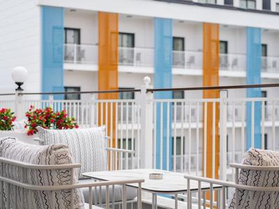 Balkon mit Sitzmöbeln vor einem Hotel mit blau-gelben Fassaden und Gauben.
