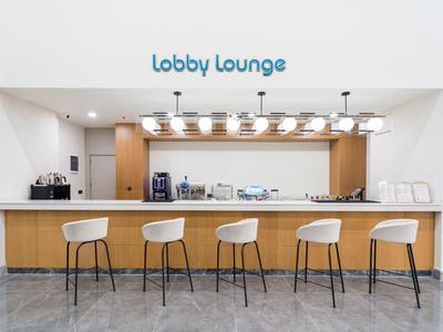 Helle Lobby Lounge mit Holztresen, fünf weißen Barhockern und moderner Beleuchtung.