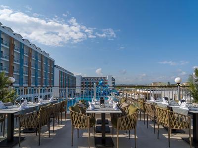 Dachterrasse mit gedeckten Tischen, modernen Stühlen und Blick auf modernes Hotelgebäude und Himmel.