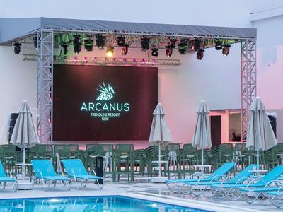 Moderner Außenbereich mit Pool, blauen Liegestühlen und großer LED-Bühne bei Sonnenuntergang.
