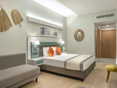 Helles Hotelzimmer mit Doppelbett, Sofa, Wanddeko und Spiegel in modernem, schlichtem Design.