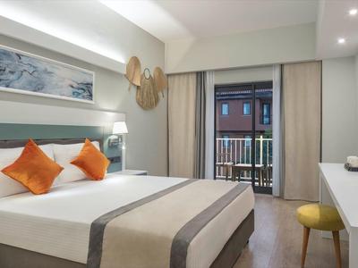 Modernes Hotelzimmer mit großem Bett, orangefarbenen Kissen, Schreibtisch und Balkon.
