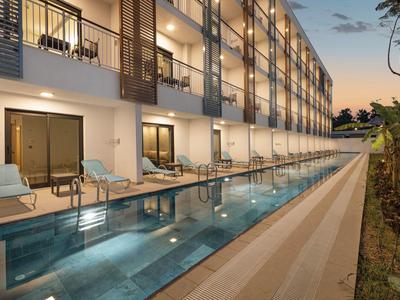 Moderner Hotelpool am Abend mit laminierten Liegestühlen und Glasgeländer an Balkonen.