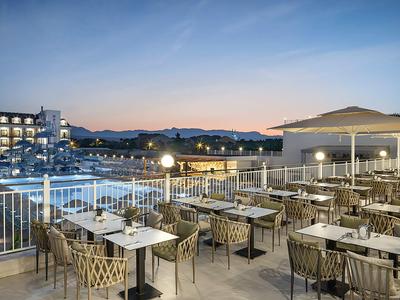 Freiluftrestaurant mit Tischen und Stühlen, Blick auf Pool und Gebäude bei Dämmerung.