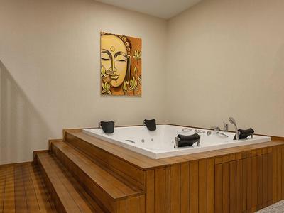 Moderner Whirlpool aus Holz mit Stufen in einer schlichten, weißen Ecke und Buddha-Bild an der Wand.