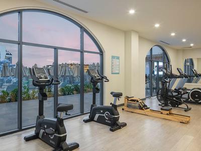 Moderner Fitnessraum mit großen Fenstern, Ergometern, Rudergerät und Holzfußboden.