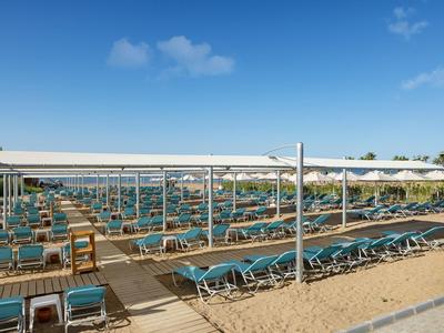 Viele blaue Liegestühle in Reihen auf einem Sandstrand unter weißen Sonnendächern bei blauem Himmel.