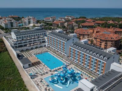 Großes Hotel mit blauen Pools, Wasserrutschen und umliegenden Wohngebäuden nahe Küste.