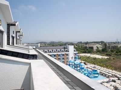 Blick von einer Hotelterrasse auf einen Poolbereich mit blauen Liegen und einer grünen Landschaft im Hintergrund.
