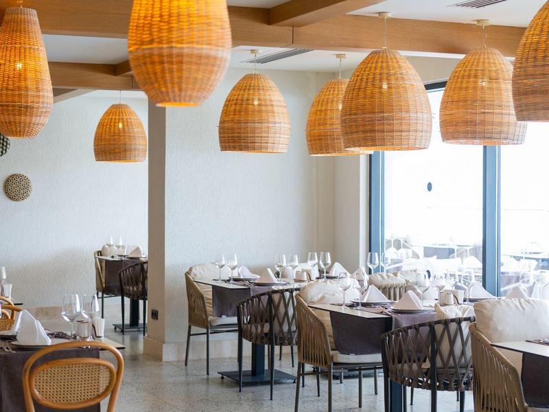 Restaurant met houten balken, rotan lampen en tafels gedekt met witte tafelkleden en bestek.