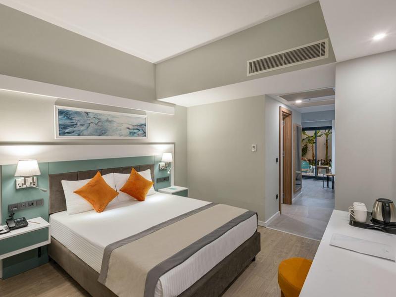 Modern hotelkamer met tweepersoonsbed, oranje kussens en bureau met waterkoker.