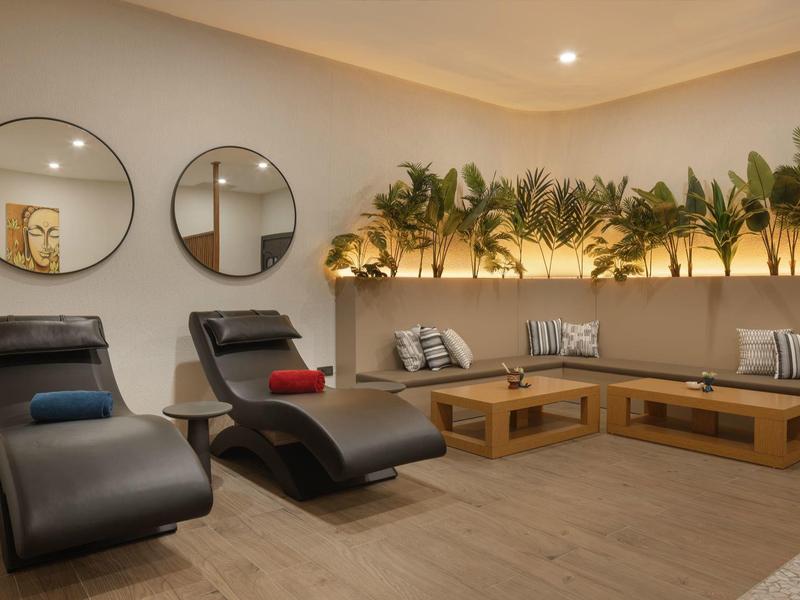 Modern wellnessruimte met zwarte ligstoelen, spiegels en verlichting onder planten.