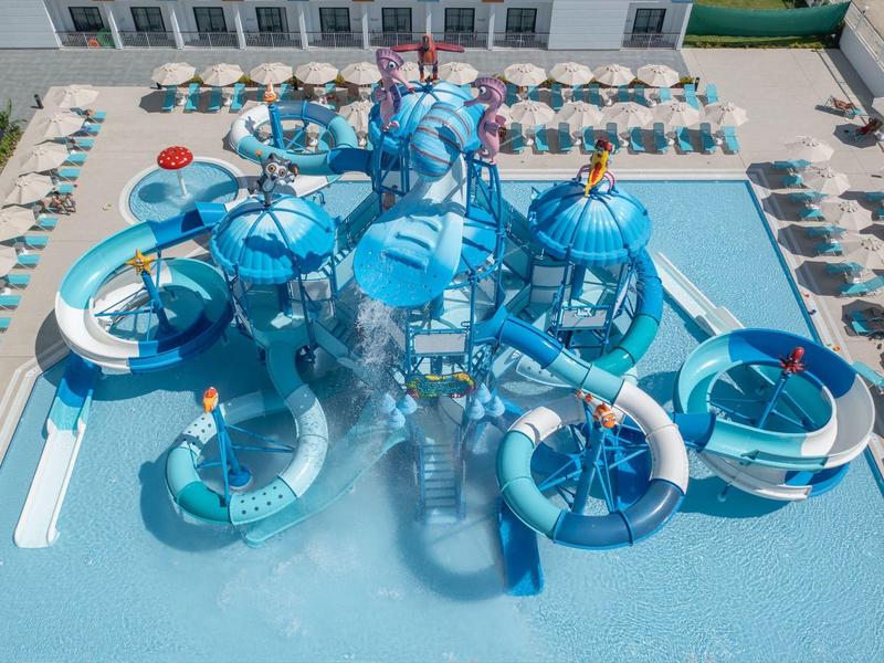 Waterpark met blauwe glijbanen en waterspelletjes in een zwembad omringd door ligstoelen.