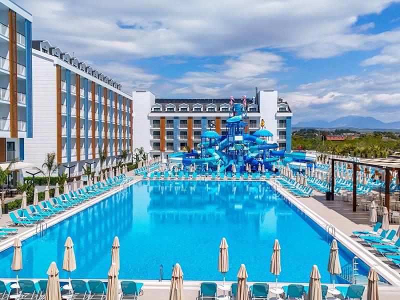 Groot hotel met groot buitenzwembad, glijbanen en ligbedden onder een blauwe lucht.