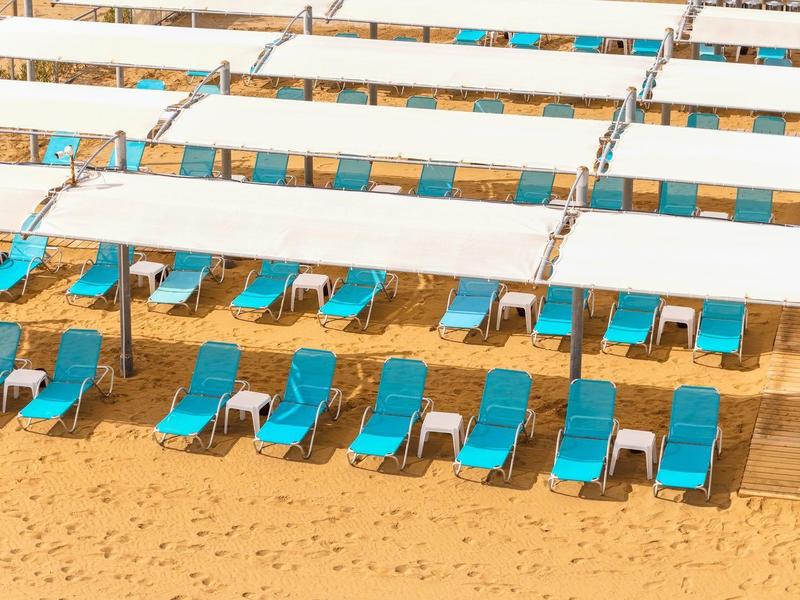 Meerdere rijen blauwe ligstoelen onder witte zonneschermen op een zandstrand.