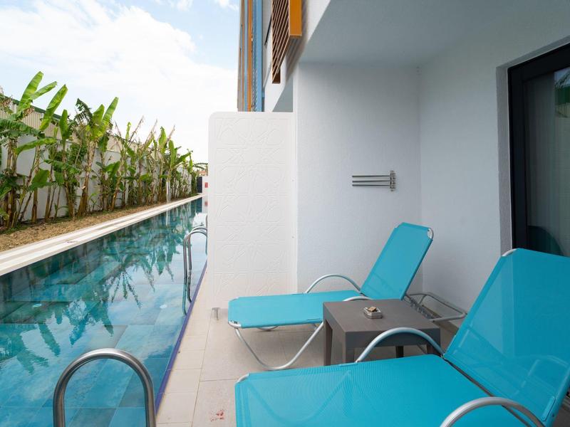 Twee blauwe ligstoelen naast een smal zwembad op een hotelbalkon.