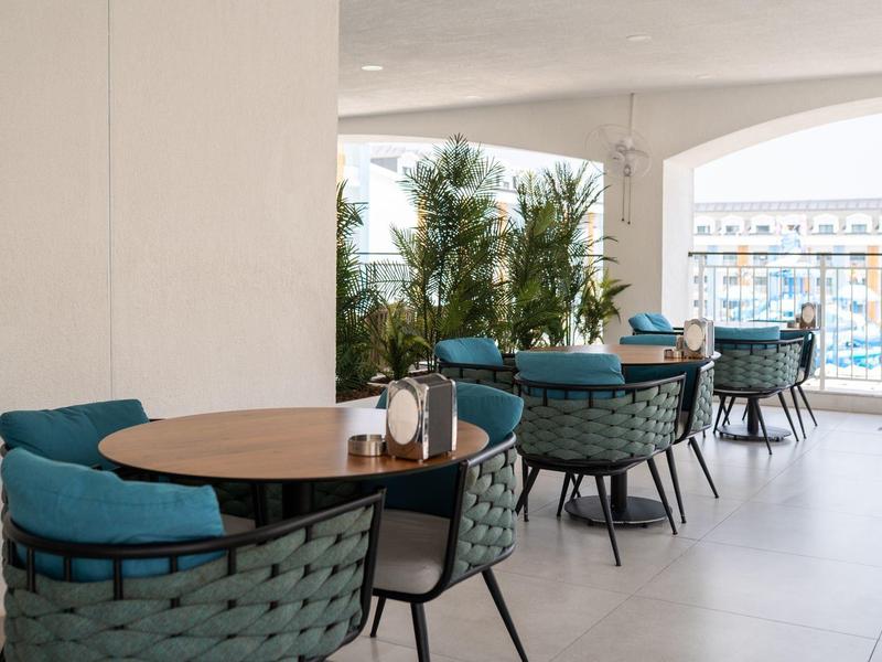 Moderne zithoek met blauwe stoelen en houten tafels naast grote ramen.