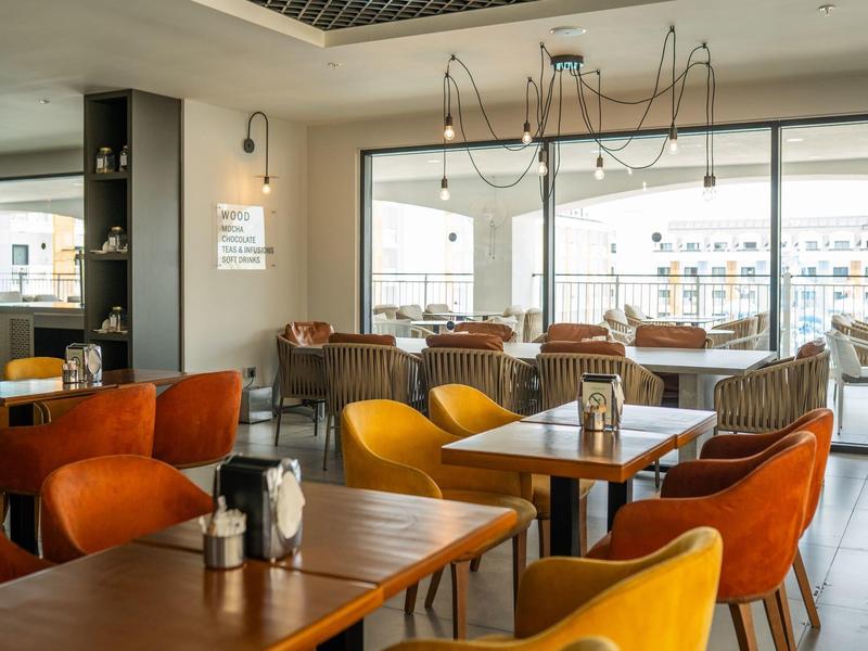 Modern hotelrestaurant met kleurrijke stoelen en grote ramen met uitzicht op een terras.