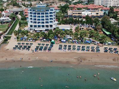 Strand mit Liegen, Sonnenschirmen, Hotelgebäude und grünem Garten an der Küste.