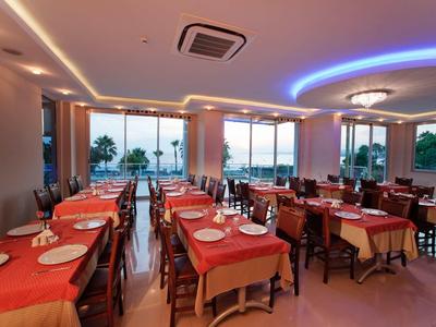 Restaurant mit gedeckten Holztischen, orangen Tischdecken und großem Fenster mit Blick auf Palmen.