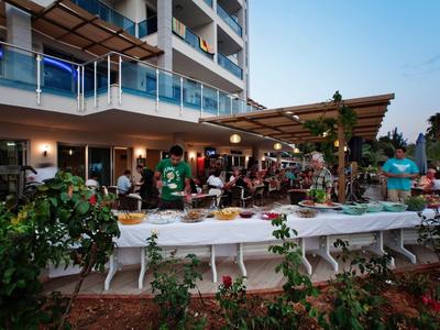 Menschen versammeln sich abends auf einer Terrasse eines modernen Gebäudes mit Tischen und Beleuchtung.
