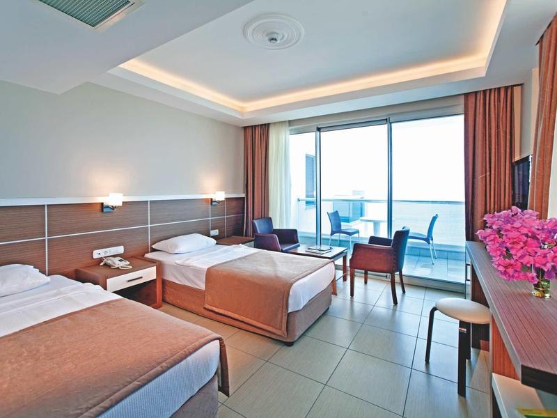 Habitación de hotel moderna con dos camas individuales, balcón y vista al mar a la luz del día.