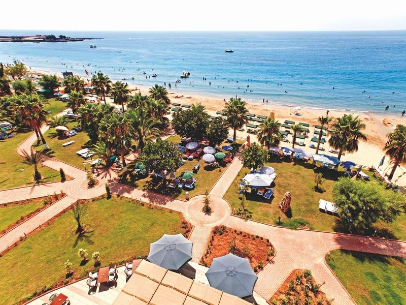 Vista aérea de una playa concurrida con palmeras, senderos y el mar azul al fondo.