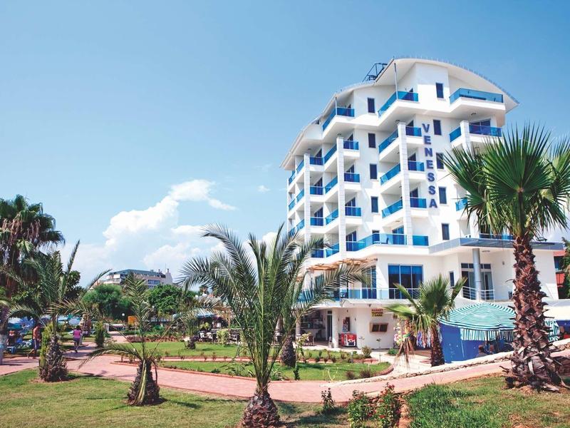 Edificio moderno de hotel blanco con balcones azules rodeado de palmeras bajo un cielo despejado.