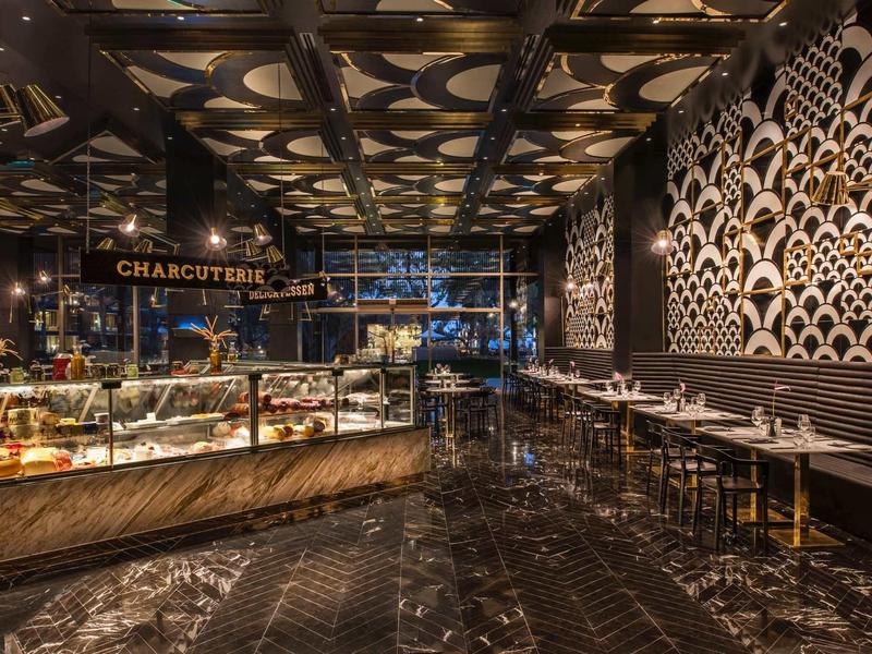 Tmavý a elegantní interiér lahůdkářství s proskleným pultem a dřevěnými stoly.