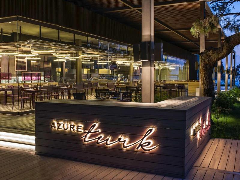 Moderní vstup do restaurace baru s neonovým osvětlením a výhledem na moře za soumraku.