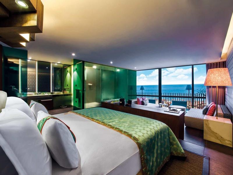 Moderní hotelový pokoj s výhledem na moře a skleněnou koupelnou.