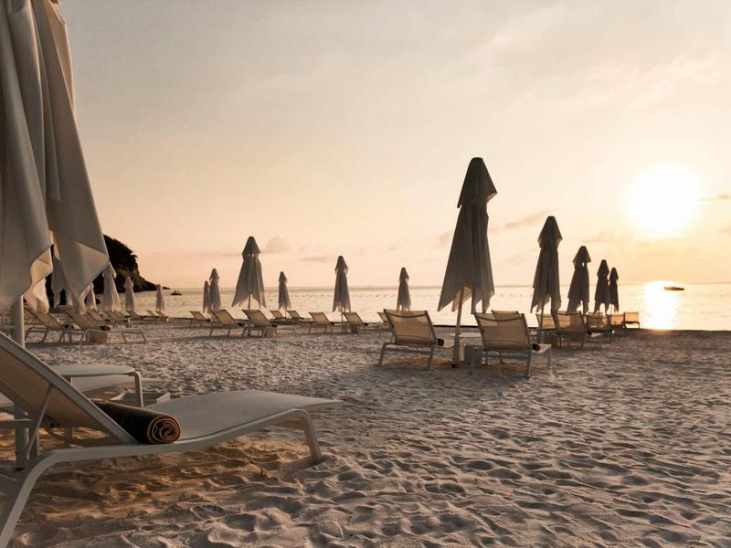 Pláž s lehátky a zavřenými slunečníky při západu slunce.