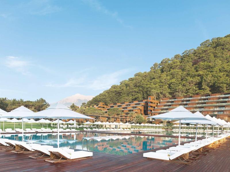 Venkovní bazén s bílými lehátky a zalesněnými kopci v pozadí.