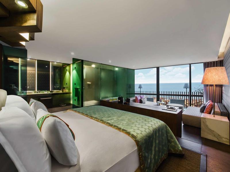 Elegantní hotelový pokoj s velkou postelí, výhledem na moře a moderním obývacím koutem.