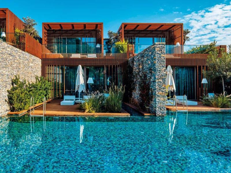 Moderní vila s bazénem a kamennými zdmi pod jasnou modrou oblohou.