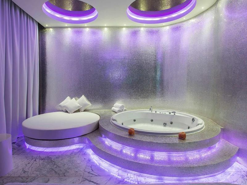 Luxusní koupelna s kulatou vanou a fialovým osvětlením.
