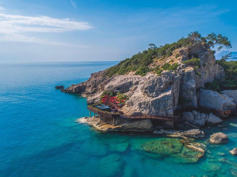 Skalnatý ostrůvek s budovou s červenou střechou obklopenou průzračnou tyrkysovou vodou.
