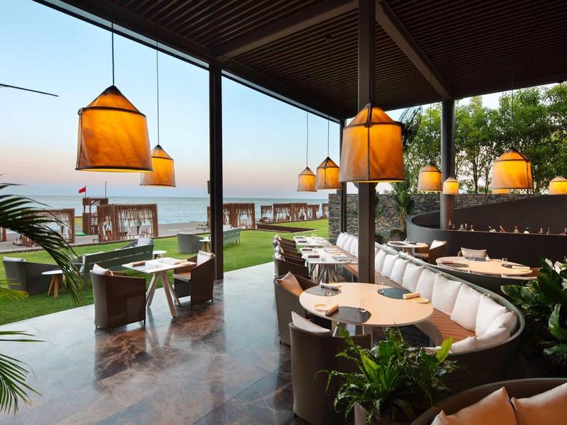 Elegantní terasa restaurace s visícími lampami a výhledem na moře při západu slunce.