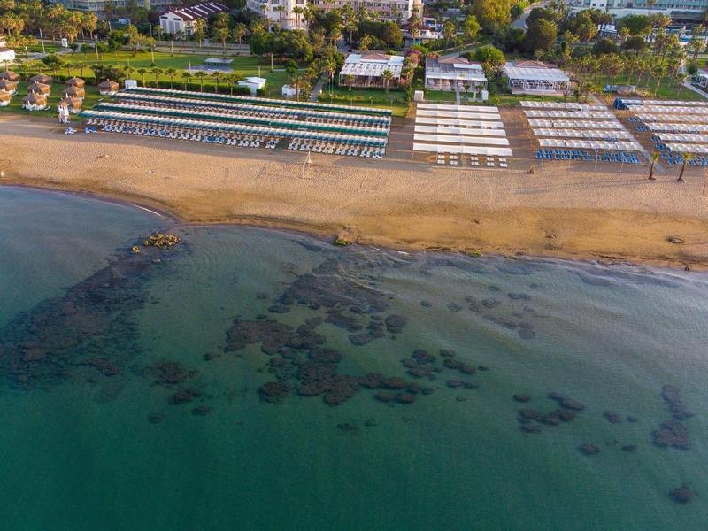 Letecký pohled na pláž s terasou a slunečníky u břehu.