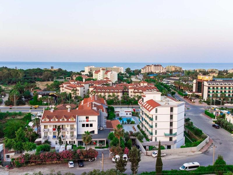 Panoramatický pohled na hotelový komplex s několika budovami, bazény a palmami u moře.