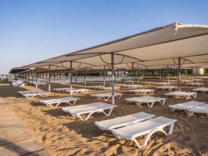 Prázdné bílé lehátka pod velkými slunečníky na pláži za jasné oblohy.