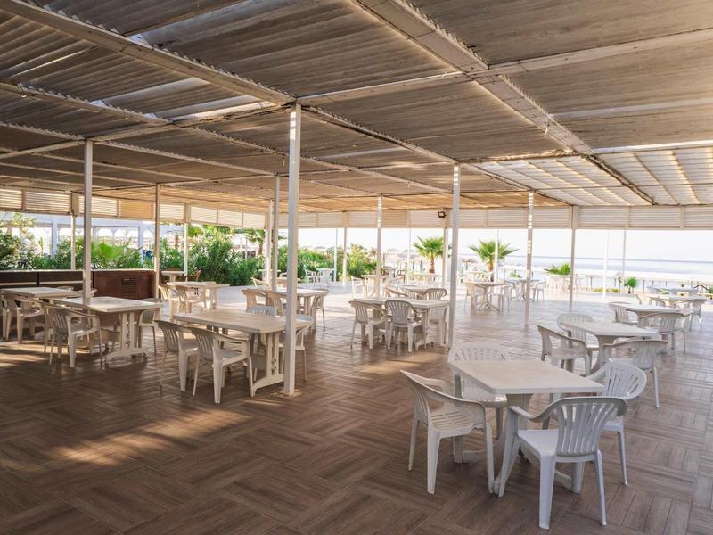 Otevřená zastřešená venkovní terasa s bílými stoly a židlemi v hotelové restauraci.