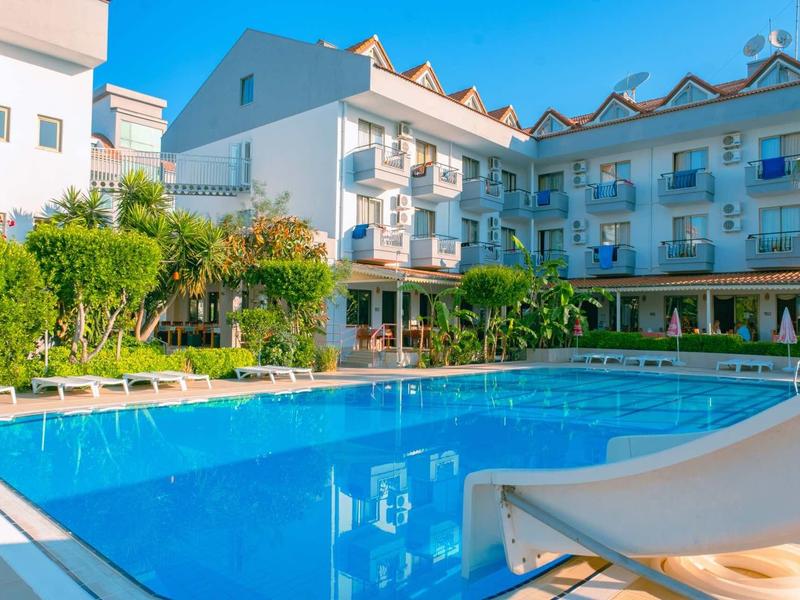 Hotel s velkým venkovním bazénem, lehátky a bílými budovami pod modrou oblohou.