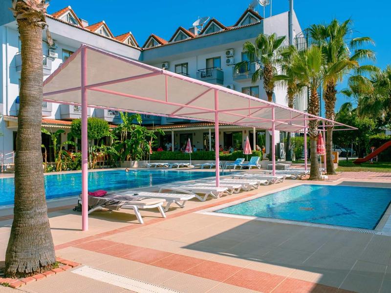 Moderní bazénová oblast s lehátky, palmami a slunečníky před hotelovou budovou.