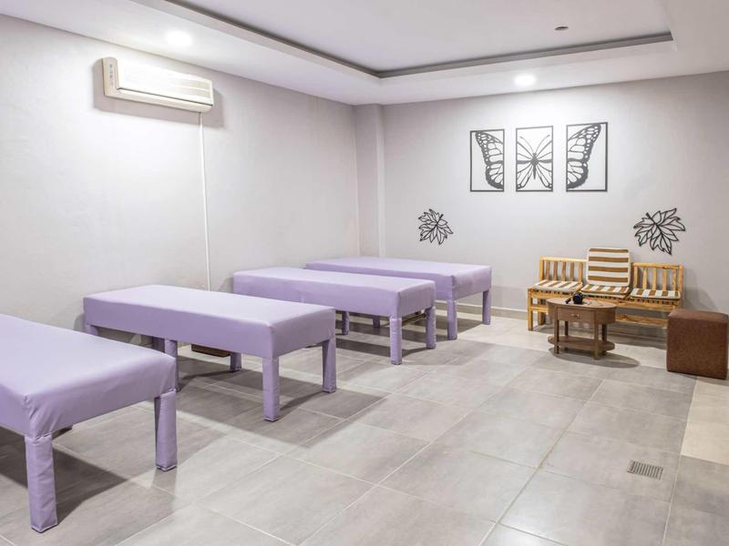 Světelná masážní místnost se třemi fialovými lehátky a posezením s dřevěnou lavicí a stolem.